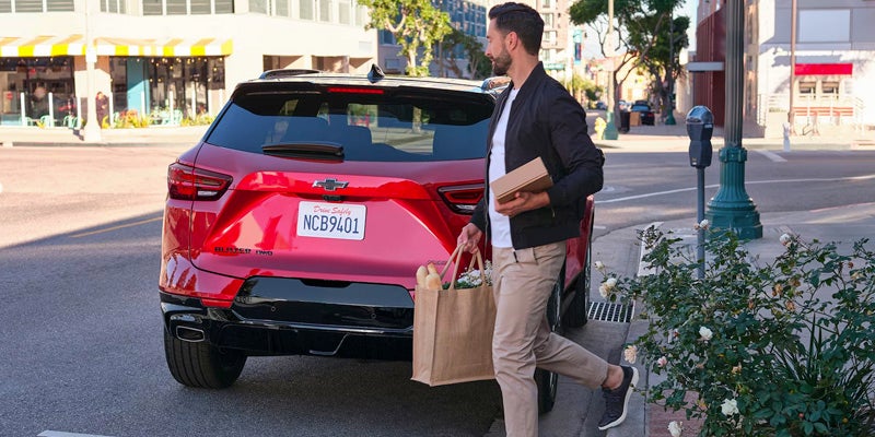 A men holding bag and box in hand walking towards red Chevrolet Blazer