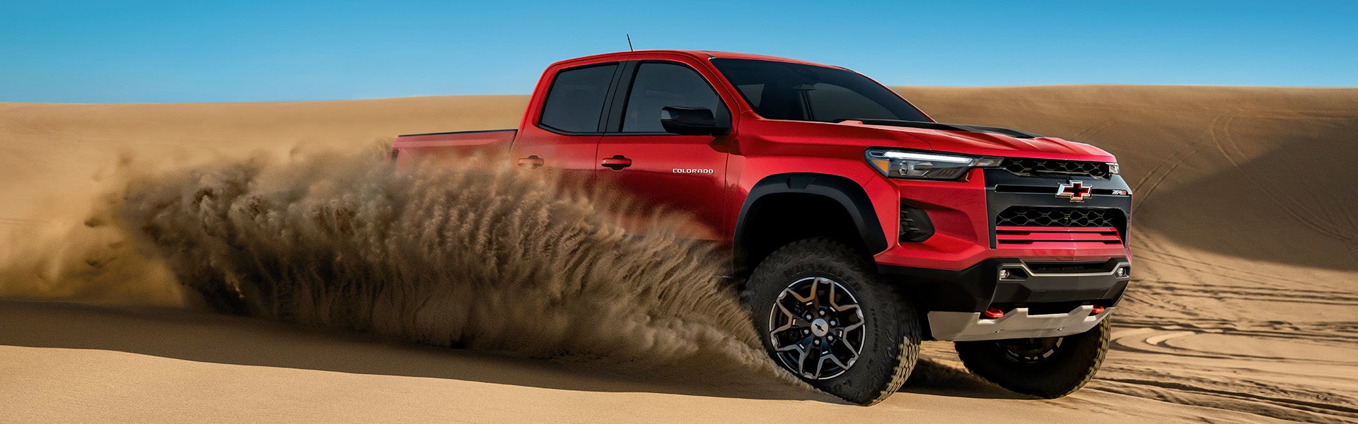 Red Chevrolet Colorado truck kicking up sand in desert