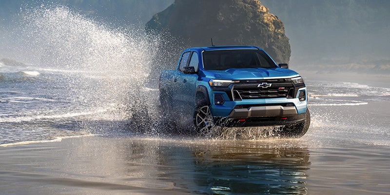 Blue Chevrolet Colorado truck splashing through ocean water