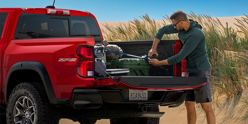 A men is fitting a luggage in trunk of Chevrolet Colorado in desert near grass