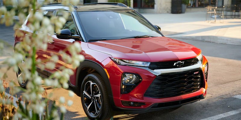 Red Chevrolet Trailblazer parked near sidewalk with plants in foreground