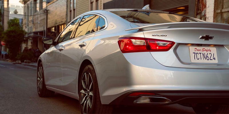 Silver Chevrolet Malibu parked one side of city road front of buildings