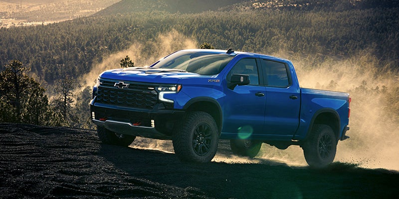 Blue Chevrolet Silverado climbing on black soil road near jungle