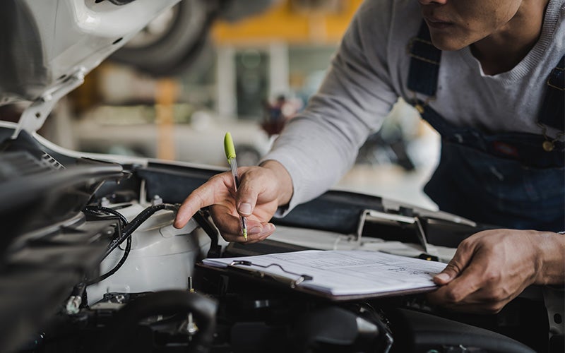 Technician checking car engine with notepad